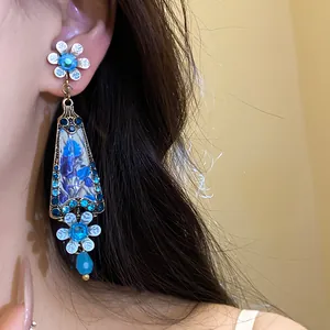 Close-up of vintage palace style earrings with blue resin floral drops and rhinestones.