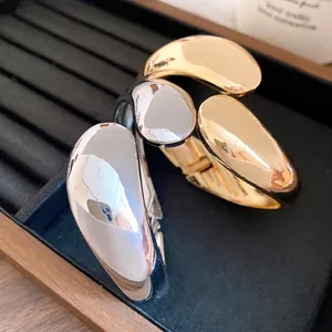 Minimalist twisted teardrop bangles in polished gold and silver metallic finishes.