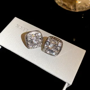 Dettaglio di orecchini a lobo quadrati argentati con pietre trasparenti brillanti.