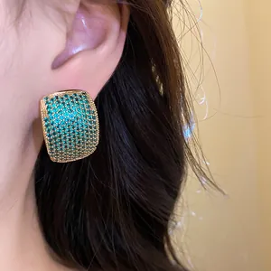 Detail macro view of vintage C-shaped gold earring encrusted with green pavé zirconia