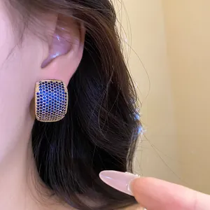 Close-up of vintage C-shaped stud earrings with blue zircon stones on model's ear
