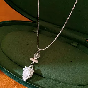 Detailed close-up of a silver pinecone pendant necklace inside a green velvet jewelry box.