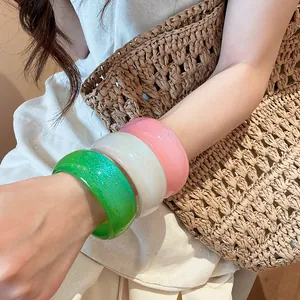 Close-up of colorful resin chunky bracelets with glitter finish on a model's arm.