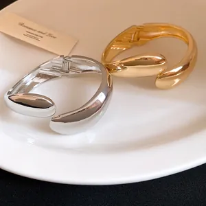 Detailed view of polished gold and silver twisted water drop hinged bangles