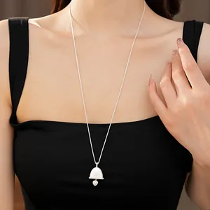 Elegant silver bell and heart charm long necklace pendant shown on a black top.