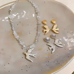 Macro detail view of swallow earrings and necklace jewelry set on a textured ceramic plate