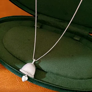 Close-up of silver bell pendant necklace with heart charm in a green jewelry box.