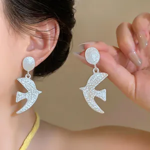 Macro view showing the hammered texture of matte silver swallow earrings on model