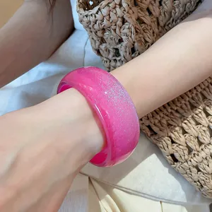 Detail of a wide pink resin bangle with silver glitter worn by a model in sunlight