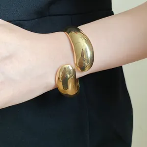 Detailed close-up of a chunky gold-tone twisted water drop cuff bracelet on model's wrist