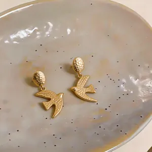 Close-up view of matte gold swallow stud earrings with textured hammer-finish detail.