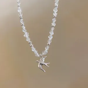 Detail view of a minimalist silver swallow bird pendant necklace with clear faceted beads.