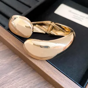 Close-up of a chunky gold teardrop bangle with a polished finish and hinged opening.