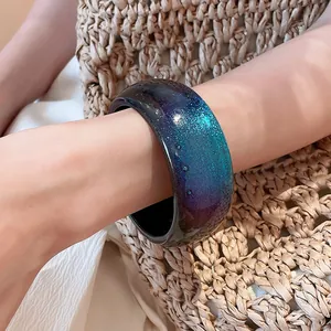 Macro detail of a chunky resin bangle featuring a purple and teal starry galaxy glitter design