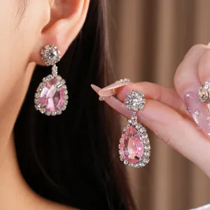 Close-up of elegant pink teardrop earrings with a sparkling rhinestone halo on ear