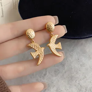 Macro view of gold swallow earrings with hammered texture and matte finish.