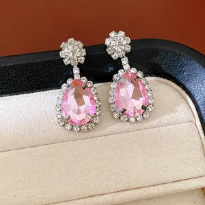 Close-up of elegant pink pear-shaped drop earrings with a sparkling rhinestone halo.