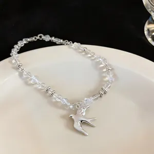 Detail view of a silver swallow pendant necklace with transparent beads on white plate