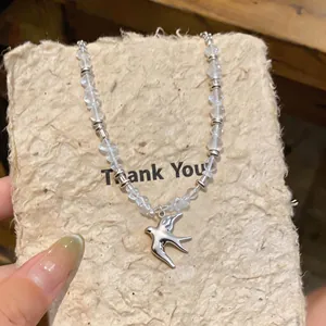 Detail shot of a matte silver swallow pendant necklace with clear beads on a textured board.