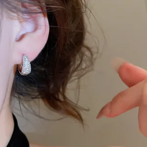 Detailopname van 14K vergulde oorring met pavé gezette zirkoon aan de oorlel gedragen.