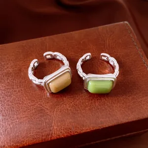 Detailed view of two minimalist geometric open rings with beige and green resin stones