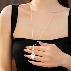 Detailed view of a silver heart pendant necklace with glass stone accents on a long chain.
