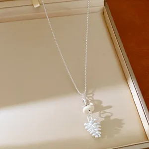 Close-up of a silver-tone necklace with a unique white pinecone and glass bead pendant