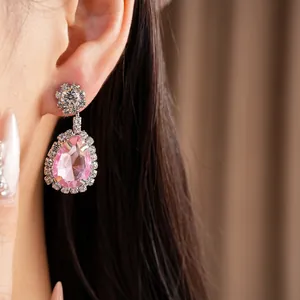 Close-up of pink teardrop crystal earring with elegant diamond-like halo on ear.