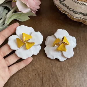 Detailansicht der übergroßen Emaille-Blumenohrringe in Weiß und Gelb auf dunklem Holzhintergrund.