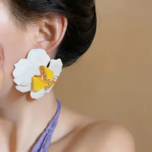 Nahaufnahme von übergroßen weiß-gelben Emaille-Blumenohrringen an einem Modell