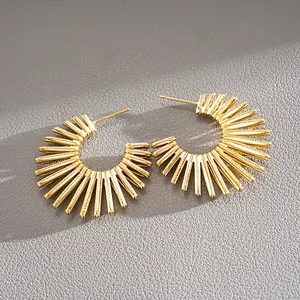 Detailed close-up of gold sunburst C-shaped hoop earrings on grey textured leather background.