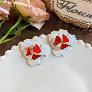Nahaufnahme eleganter weißer Blumenohrringe mit roten Akzenten auf einem Keramikteller