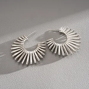 Close-up of silver-tone C-shaped hoop earrings with sunburst spike design details.