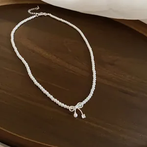 Elegante Perlenkette mit Schleifenanhänger und funkelndem Tropfen.
