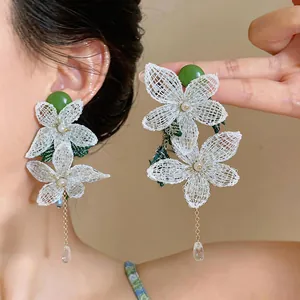 Detailed view of white mesh flower earrings with green accents and dangling beads