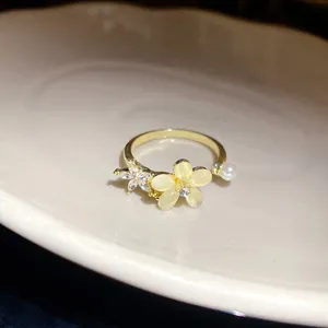 Dettaglio di un anello aperto dorato con fiori in occhio di gatto e una piccola perla.