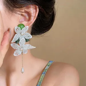 Detailed view of elegant white lace flower earrings with dangling pearl on a model