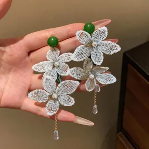 Detailed view of white mesh flower earrings with green beads and pearl teardrops