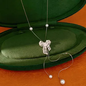 Detailed view of silver hollow bow necklace with pearls in a green jewelry box
