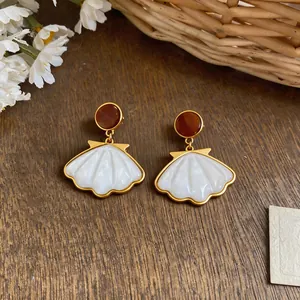 Elegant shell-shaped drop earrings with gold trim on a rustic wooden background