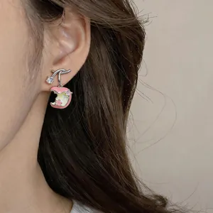 Close-up of elegant silver apple earrings with pink enamel and zircon on an ear.