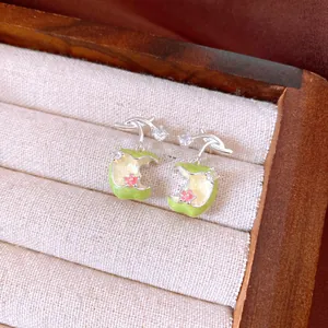 Close-up of elegant green apple earrings with zircon stones in a wooden jewelry box.