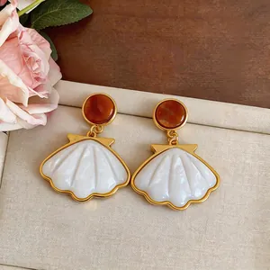 Close-up of elegant gold-toned shell pendant earrings with amber resin studs