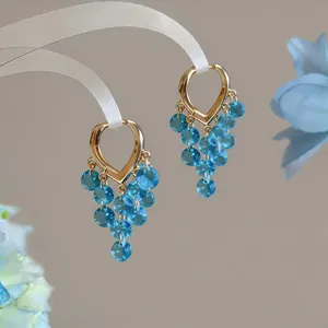 Detailansicht goldener Herz-Ohrringe mit kaskadierenden blauen Kristallperlen-Quasten.
