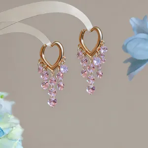 Nahaufnahme goldener herzförmiger Creolen mit hängenden rosa Kristallquasten.