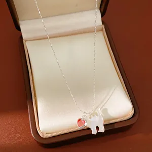 Dettaglio di una collana d'argento con un cuore rosso e un ciondolo a gatto bianco.