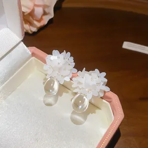 Detail view of white flower cluster earrings with clear resin waterdrop pendants