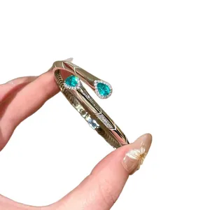 Elegante bracciale rigido dorato aperto con zirconi blu a goccia e dettagli in pavé