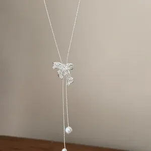 Macro view of silver hollow bow necklace featuring zircon stones and pearl tassels