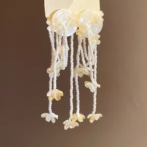 Close-up of white seed bead tassel earrings with delicate resin flower charms.